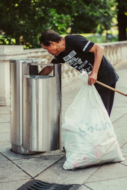 A large pile of black rubbish bags, some partially open revealing plastic bottles and discarded waste, is situated outdoors in front of a modern building with tiled exterior walls. The bags are stacke