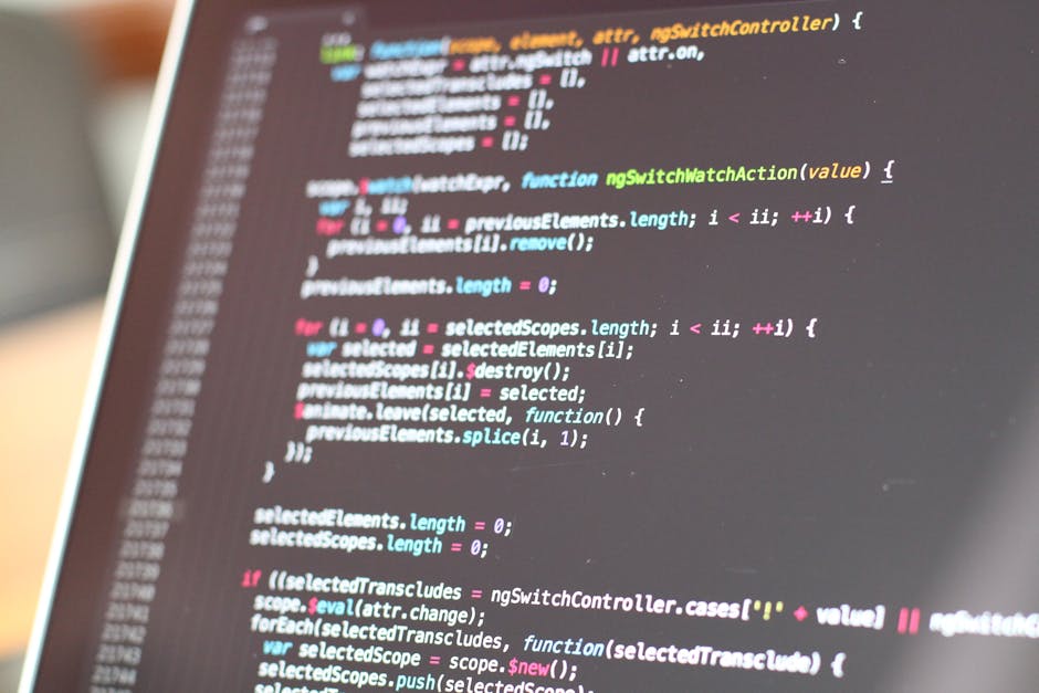 A close-up image of an open laptop displaying lines of programming code on its screen, positioned on a wooden surface. To the right of the laptop is a coffee mug with a beige background and black text